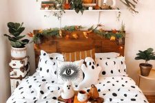 a fall to Halloween bedroom with a stained bed with an evegreen and leaf garland, leaves and a pumpkin on the shelf and fall leaves and gourds on the bed