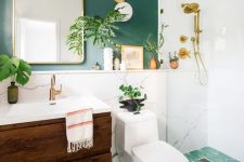a farmhouse bathroom with a green accent wall, a green tiled floor, a dark stained floating vanity and potted plants plus gilded touches