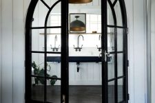 a farmhouse space with black frame arched double doors, a black floating sink and black pendant lamps, vintage fixtures is chic