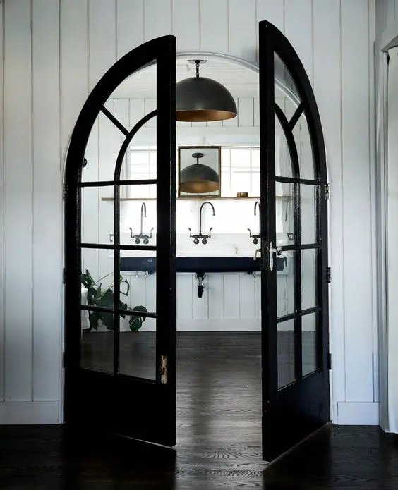 a farmhouse space with black frame arched double doors, a black floating sink and black pendant lamps, vintage fixtures is chic