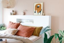 a fresh Scandinavian bedroom with a blush accent wall, a neutral bed with colorful bedding, a white headboard with a niche, a woven pendant lamp