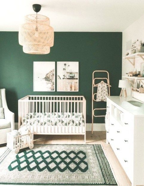 a gender neutral nursery with a dark green accent wall, neutral furniture, open shelves, a woven pendant lamp, a bold green printed rug