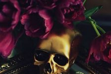 a glam gold skull paired with purple blooms is a stylish idea for decorating your space for Halloween and it looks bright and shiny