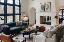 a gorgeous living room with an arched window, wooden beams, a double-sided fireplace, a black and a neutral sofa, a black coffee table and leather chairs