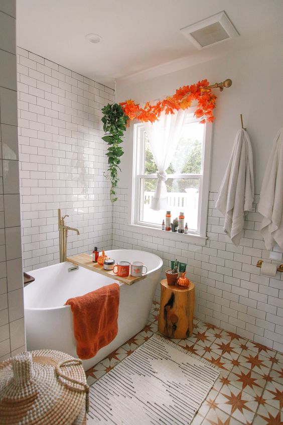 a lively fall bathroom with a tree stump side table with a faux pumpkin, an orange towel, green and orange garlands and cute pumpkins and bold mugs is amazing