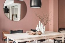 a lovely dining space with a dusty pink accent wall, a wooden table, black chairs and a bench, a pendant lamp and a round mirror is cool