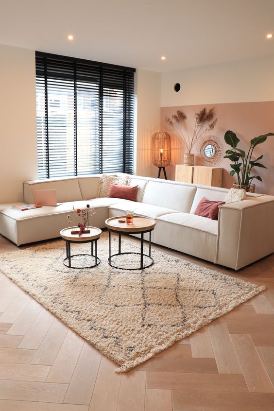 a lovely living room with a pink and white color block wall, a white sectional, a duo of coffee tables, potted plants and a mirror in a wooden frame