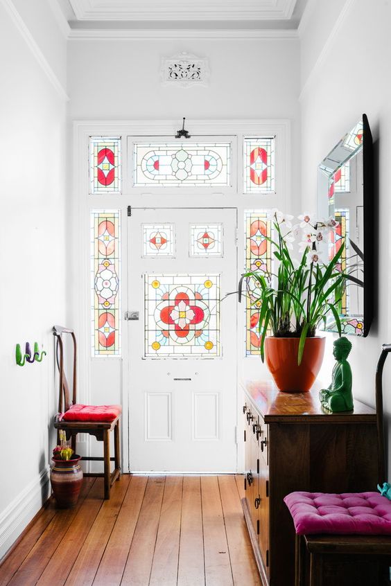 a lovely modern entryway with a door with stained glass and sidelights, too, jewel-tone chairs and a modern dresser with a planter