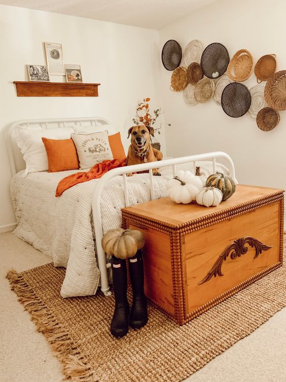 a lovely rustic fall bedroomw ith a white forged bed, a wooden chest that doubles as a bench, faux and fabric pumpkins, decorative baskets and fall leaves