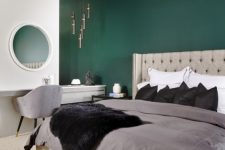 a master bedroom with a green accent wall, a grey upholstered bed, neutral bedding, a vanity with a grey chair and a white dresser