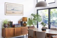 a mid-century modern dining room with lovely stylish furniture, potted plants, an exit to the garden and a clerestory window to illuminate the space
