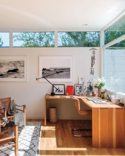 a mid-century modern home office with a glazed wall and clerestory windows, a corner desk and leather chairs is welcoming
