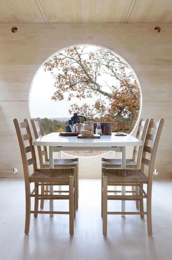a minimalist dining space with a large porthole window that is a decor feature at once as it provides amazing views and a dining set