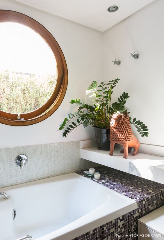 a modern bathroom with a porthole window, a bathtub clad with tiles, a stone shelf and potted greenery is a cool idea