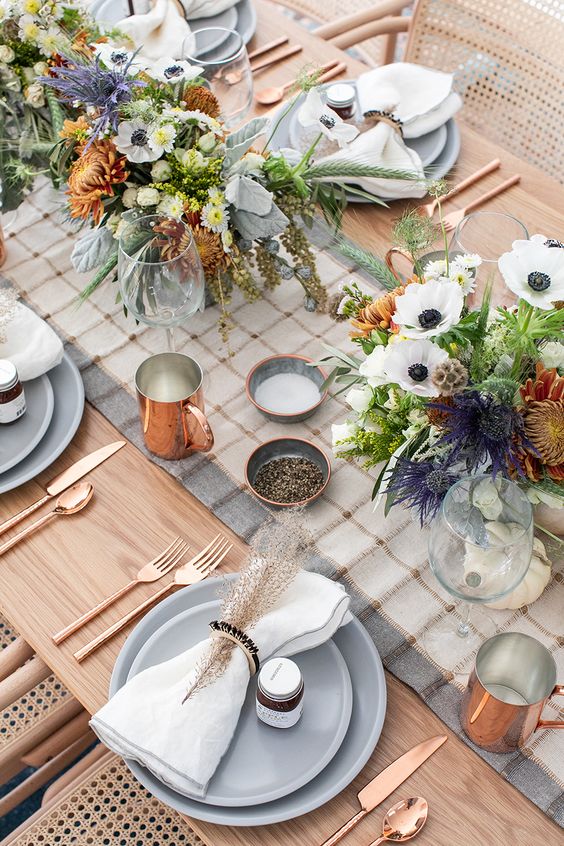 a modern farmhouse Thanksgiving tablescape with a plaid runner, neutral napkins, neutral and bold blooms and copper touches