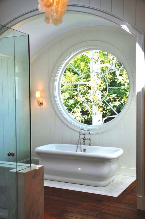 a modern farmhouse bathroom with a large porthole window next to the tub to fill the space with natural light
