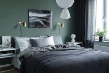 a moody bedroom with a dark green accent wall, an upholstered bed with dark bedding, white nightstands, a pendant lamp and black sheer curtains