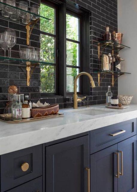 a navy home bar, a black skinny tile backsplash, glass shelves with brass bases, brass handles and fixtures is amazing