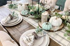 a neutral farmhouse Thanksgiving tablescape with a plaid runner and napkins, neutral and pastel pumpkins, candles and greenery is amazing
