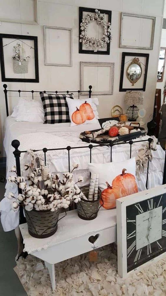 a neutral farmhouse bedroom with a gallery wall of empty frames, a forged bed, neutral and plaid bedding,a shabby chic bench, pumpkin pillows and cotton in a basket