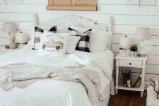 a neutral farmhouse bedroom with planked walls, a refined white bed and nightstands, neutral and plaid bedding, sunflowers, greenery and faux pumpkins