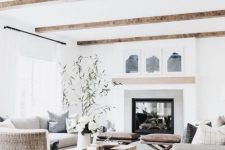 a neutral farmhouse living room with wooden beams, a large built-in fireplace, neutral seating furniture, a wooden slab table and greenery