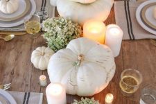 a neutral rustic Thanksgiving tablescape with an uncovered table, striped placemats, heirloom pumpkins, green hydrangeas and candles