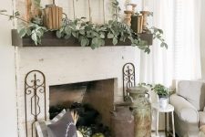 a neutral rustic mantel with greenery, books, wooden candleholders, a wood slice wreath, a tray with pumpkins and vintage churns