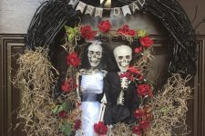 a non-traditional Halloween wreath with a just dead skeleton couple, some blooms, a bunting and hay on the wreath