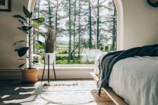 a peaceful modern bedroom with an oversized arched window for a view, a plywood bed and a fluffy rug is ultimate