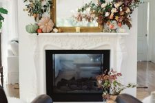 a pretty and bold fall mantel with bright and pastel pumpkins, a mirror in an ornated frame, bold leaves and blooms is a very chic idea