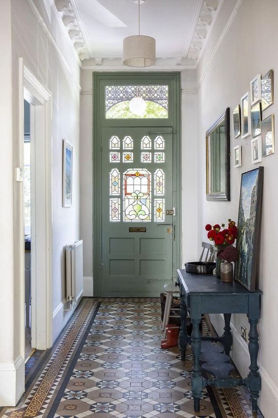 a pretty entryway with a green door with stained glass, a gallery wall, a black vanity with some art and pendant lamps