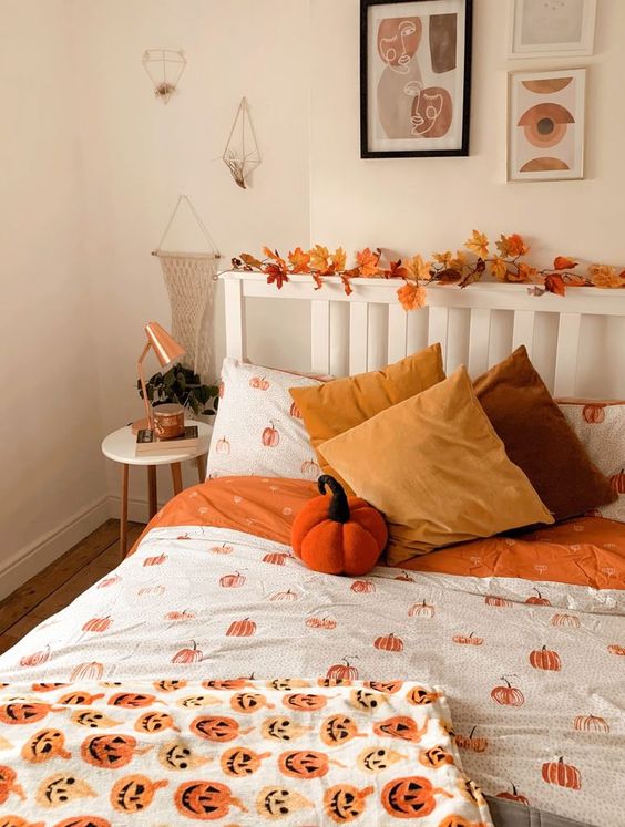 a pretty fall bedroom with a fall leaf garland interweaving the headboard, bright orange pumpkin bedding and mustard pillows, copper lamps
