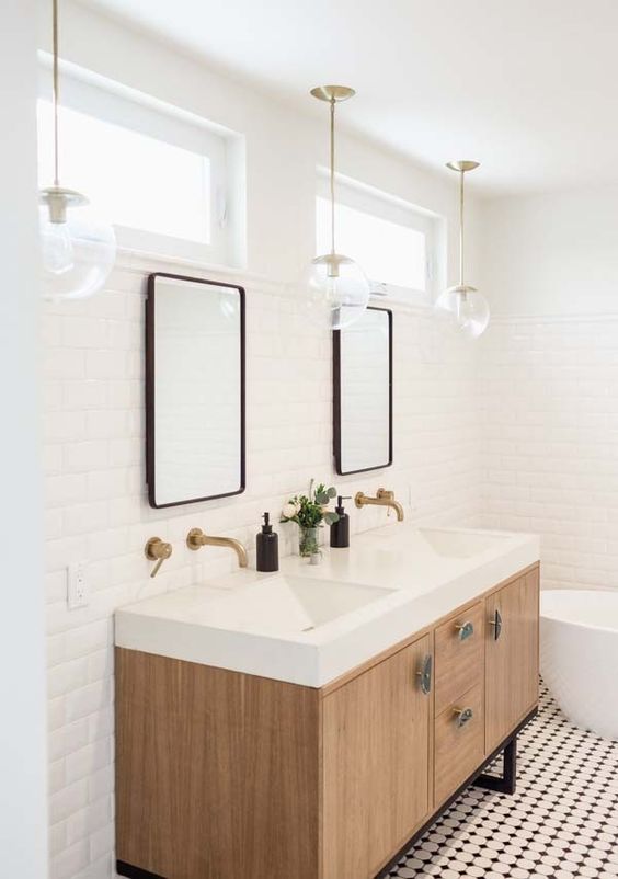 a pretty neutral bathroom with a black and white floor, a light stained vanity, an oval bathtub, two mirrors and pendant lamps