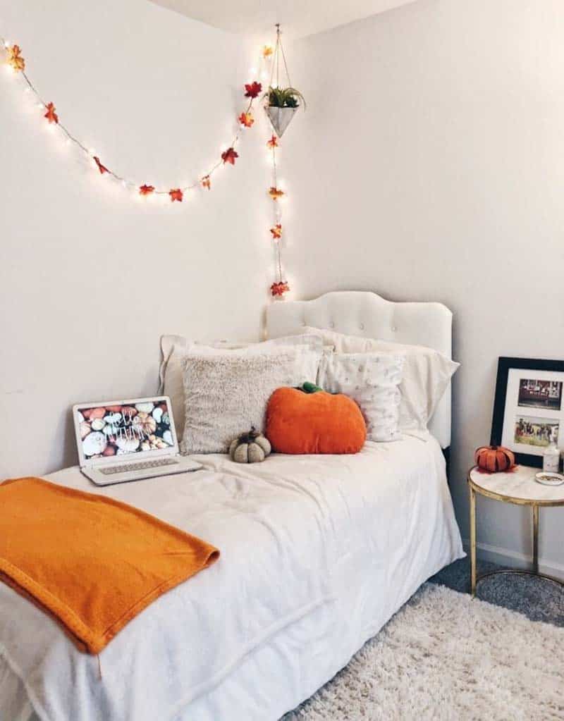 a pretty neutral bedroom styled for the fall with a leaf garland, orange blanket and pumpkin pillows is amazing