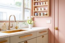 a pretty pastel kitchen with pink walls and a door, olive green cabinets, brass handles and fixtures and a brass built-in sink is super sweet