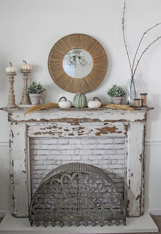 a pretty rustic fall shabby chic mantel with neutral pumpkins, pampas gras,s branches, potted greenery and a mirror in a wooden frame