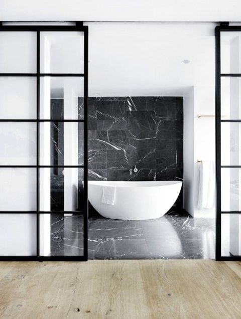 a refined contemporary bathroom done with black marble and black frame French sliding doors separating this bathroom from the rest of the apartment