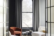a refined contemporary interior with a double-height black frame arched window, a curved sofa that echoes with it and some chairs
