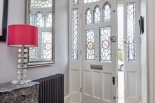 a refined entyway with stained glass sidelights and the door, a checked floor, a printed dress and a red lamp, a mirror and a black radiator