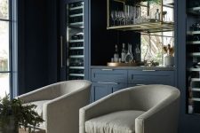 a refined living room with navy walls and a home bar, neutral chairs on brass legs, a brass glass suspended shelf is amazing