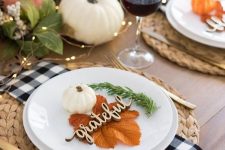 a relaxed rustic Thanksgiving table setting with wovne placemats, plaid napkins, white plates, leaves, greenery, pumpkins and lights