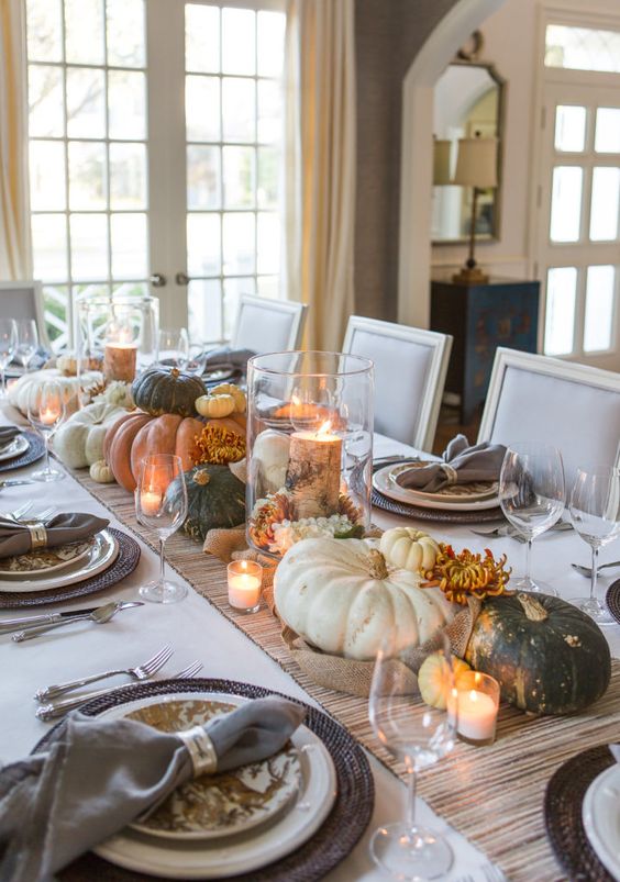 a relaxed rustic Thanksgiving tablescape with a striped runner and woven placemats, printed plates, heirloom pumpkins, candles and blooms