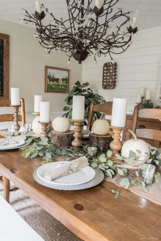 a rustic Thanksgiving table seting with white pumpkins on tree stumps, pillar candles, eucalyptus, silver chargers is chic and stylish