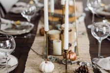 a rustic Thanksgiving tablescape with a linen table runner, pumpkins, pinecones, candles and wood slices is cool