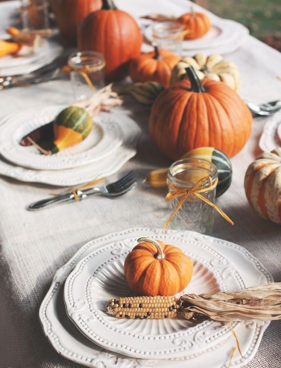 a rustic Thanksgiving tablescape with natural pumpkins, vintage plates with gourds and corn cobs and jars