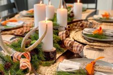 a rustic Thanksgiving tablescape with wovne placemats, antlers, pinecones, evergreens, wood slices and pilalr candles plus plaid