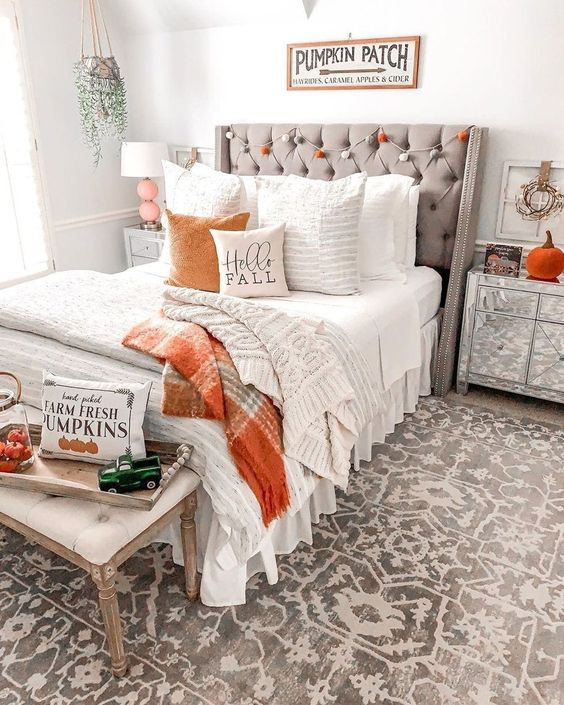 a rustic bedorom with an orange and grey pompom garland, faux pumpkins, pumpkin print bedding and plaid blankets is amazing