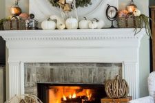 a rustic fall mantel with a greenery wreath, white pumpkins and gourds, baskets with pumpkins and greenery and some candles