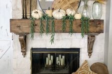 a rustic fall mantel with cascading greenery, white pumpkins, a wooden cutting board, pampas grass, black candlesticks with candles